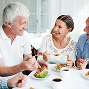Group of 4 older adults sitting around a white table enjoying dessert and coffee