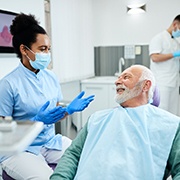 Older man in green sweater smiling at a dentist in blue scrubs