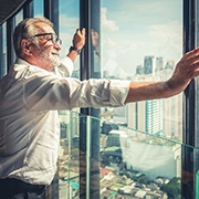 Older man in white collared shirt and glasses looking out a high-rise window